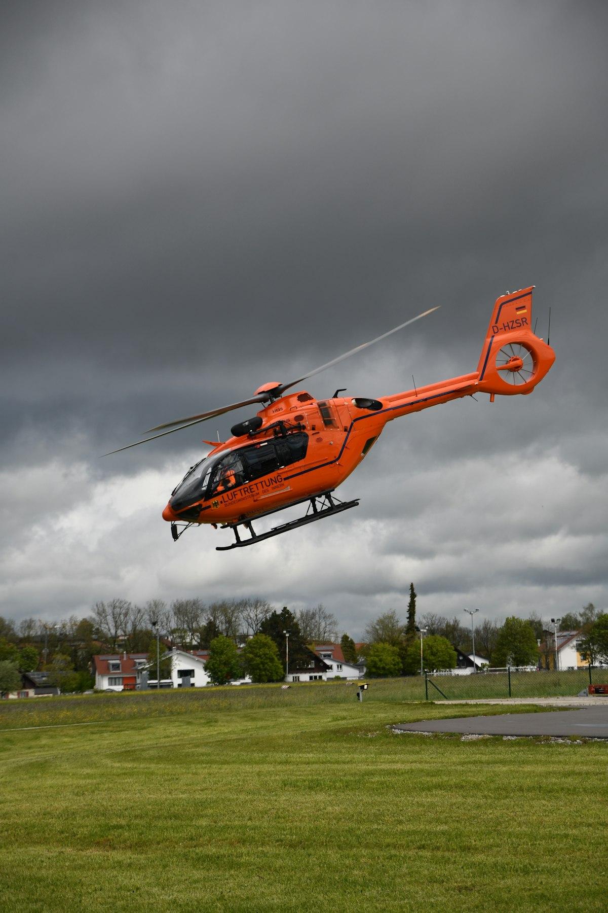 Orange helicopter flying under a cloudy sky